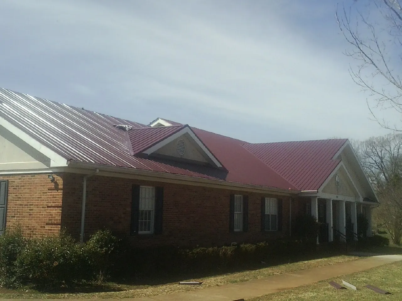 Red metal roof with gabled entries on a long brick building, from a Hail Damage Roof Repair job in Melville
